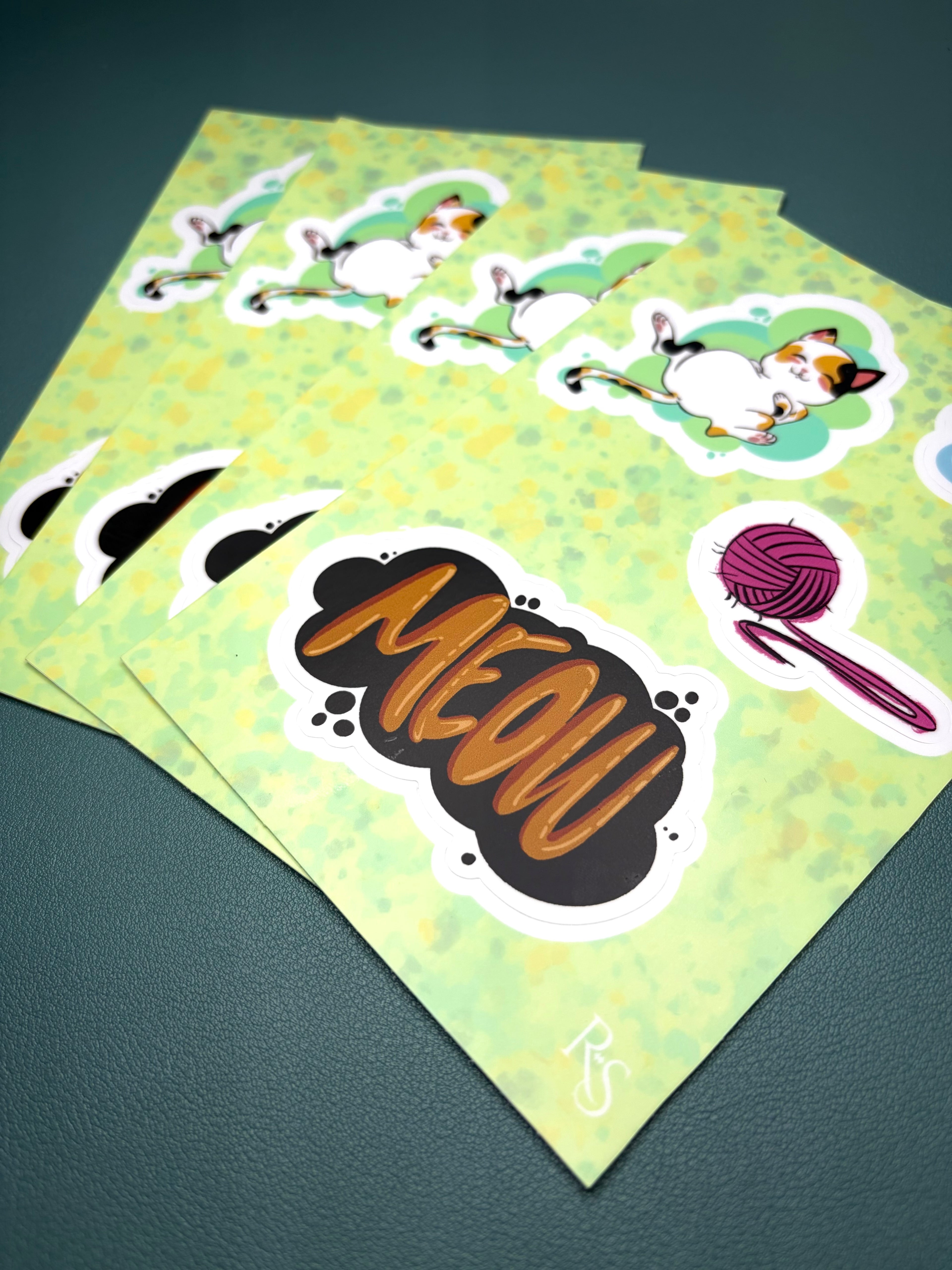 Sheet of stickers with cat designs and 'MEOW' text on a green background